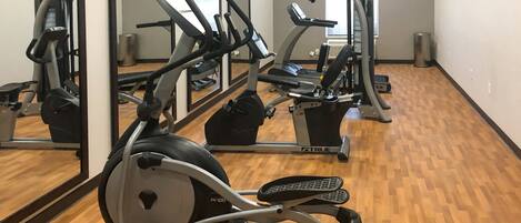 Un gimnasio con equipo de ejercicio, incluyendo cintas de correr y elípticas, y piso de madera.