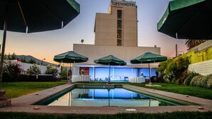 An outdoor pool area with umbrellas, a building labeled "OpenHotel," and a clear sky. - Open Hotel (Quillota)