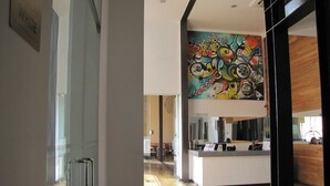 A modern hotel lobby with a reception desk, a glass door, and a colorful abstract mural on the wall. - Open Hotel (Quillota)