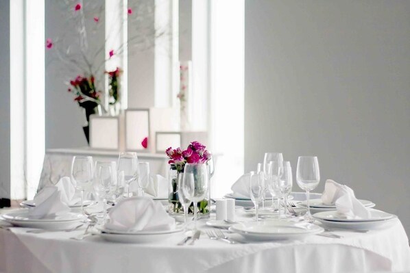 A table set for a formal dinner with white tablecloths, clear glassware, and a vase with pink flowers. - Open Hotel (Quillota)