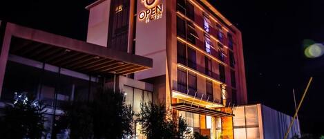 Un hotel moderno con un llamativo letrero que dice 'OPEN HOTEL', ventanas amplias y una zona de entrada cubierta.