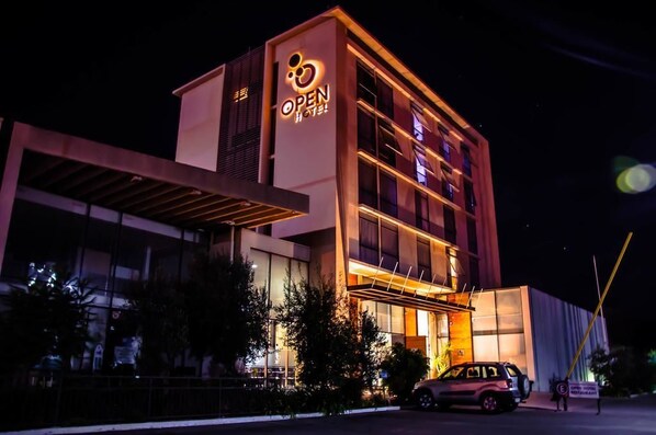 Un hotel moderno con un llamativo letrero que dice 'OPEN HOTEL', ventanas amplias y una zona de entrada cubierta.