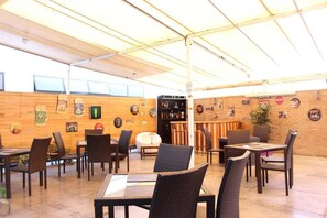 Un comedor interior con sillas y mesas de mimbre, una zona de bar con taburetes, y una pared decorada con diversos carteles y recuerdos.