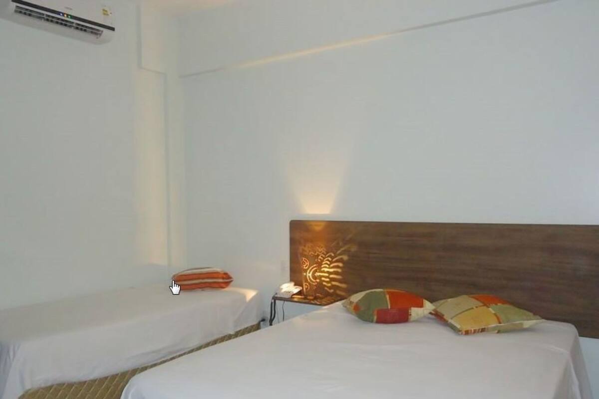 A hotel room with two single beds, a wooden headboard, a nightstand, and a wall-mounted air conditioning unit.