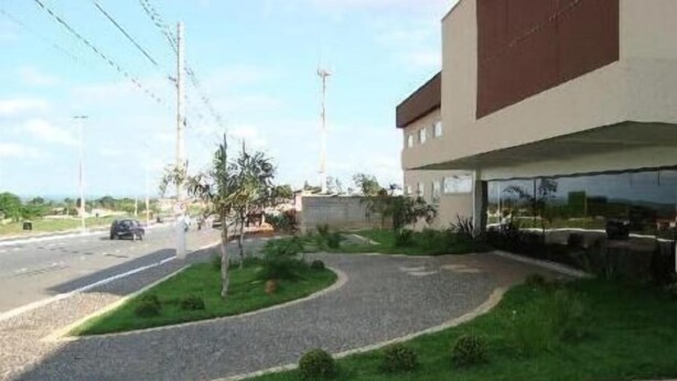 A modern building with a curved driveway, a small garden area, and a parking lot. - Senador Plaza Hotel (Senador Canedo)