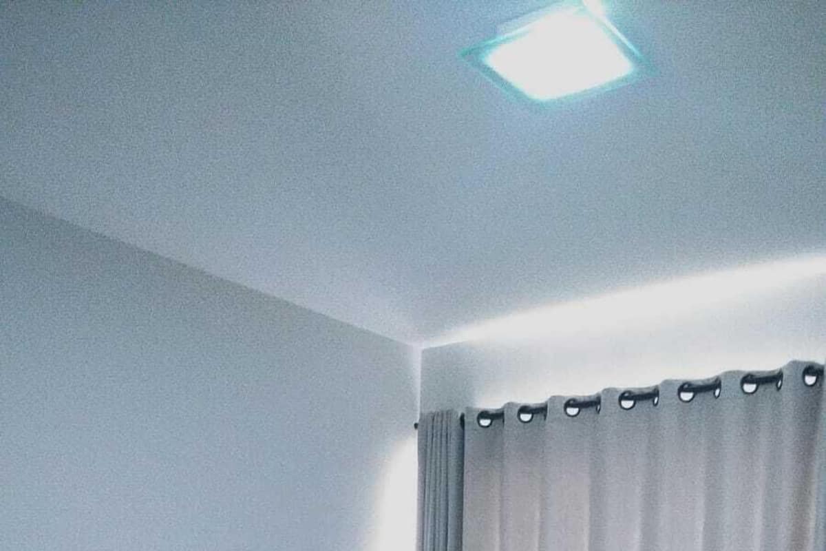 A simple, clean hotel room with a single bed, a nightstand, and a window with curtains.