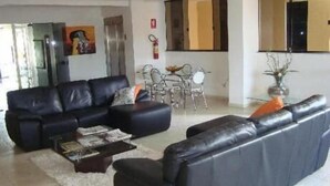 A modern living room with a black leather sofa, a coffee table, and a dining area with chairs and a table. - Senador Plaza Hotel (Senador Canedo)