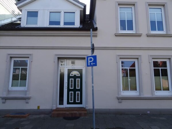 A building with a green door, white windows, and a blue parking sign.