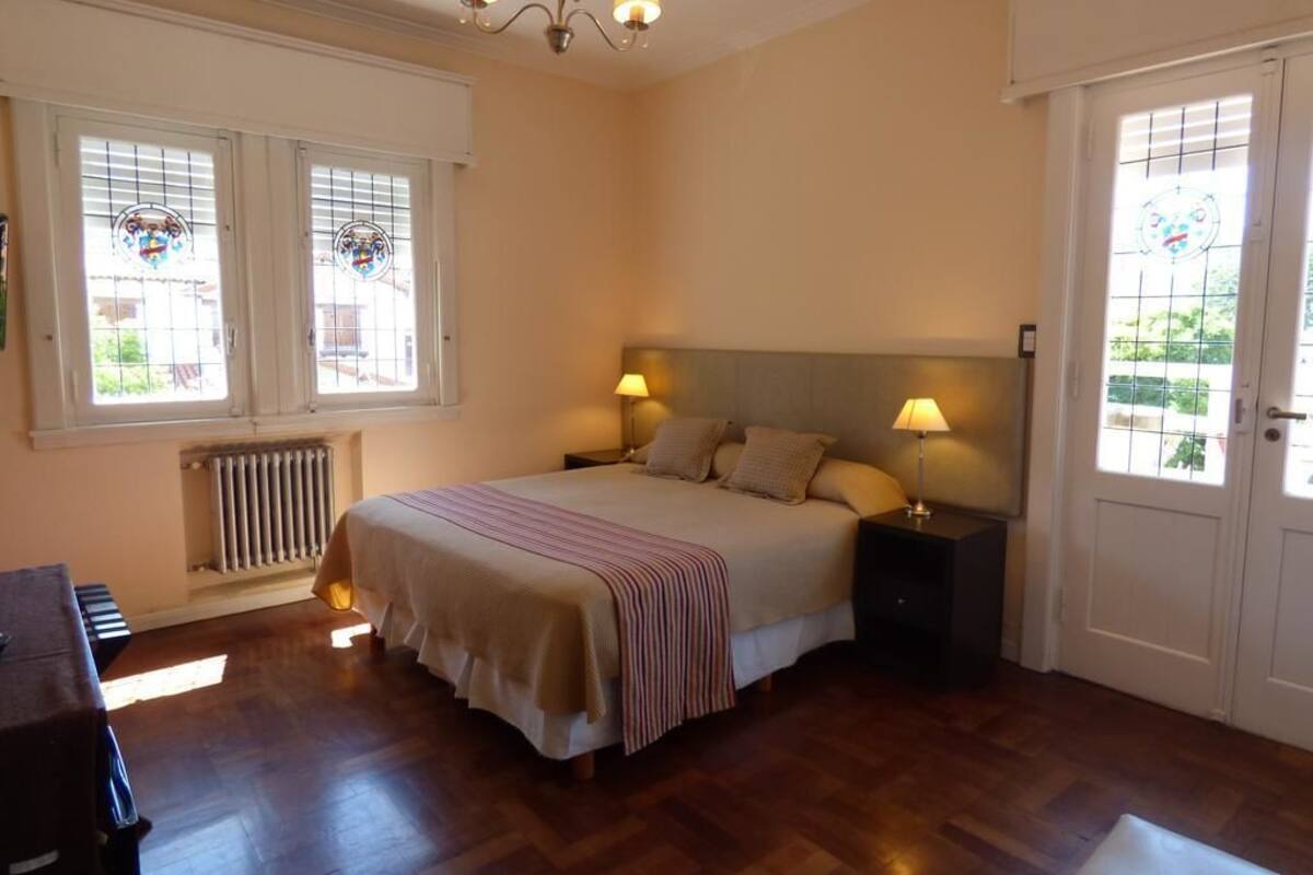 A bedroom with a bed, two bedside lamps, a radiator, and a window with a view.