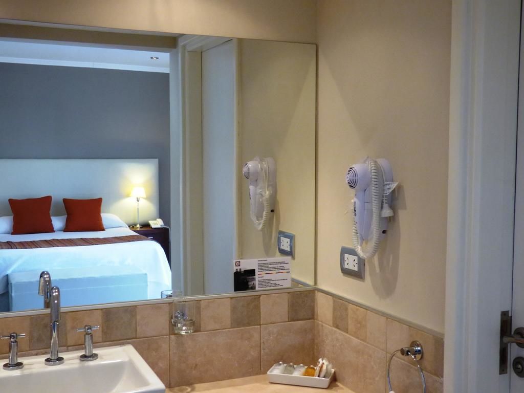 A hotel bathroom with a large mirror, a sink, and two hair dryers mounted on the wall.