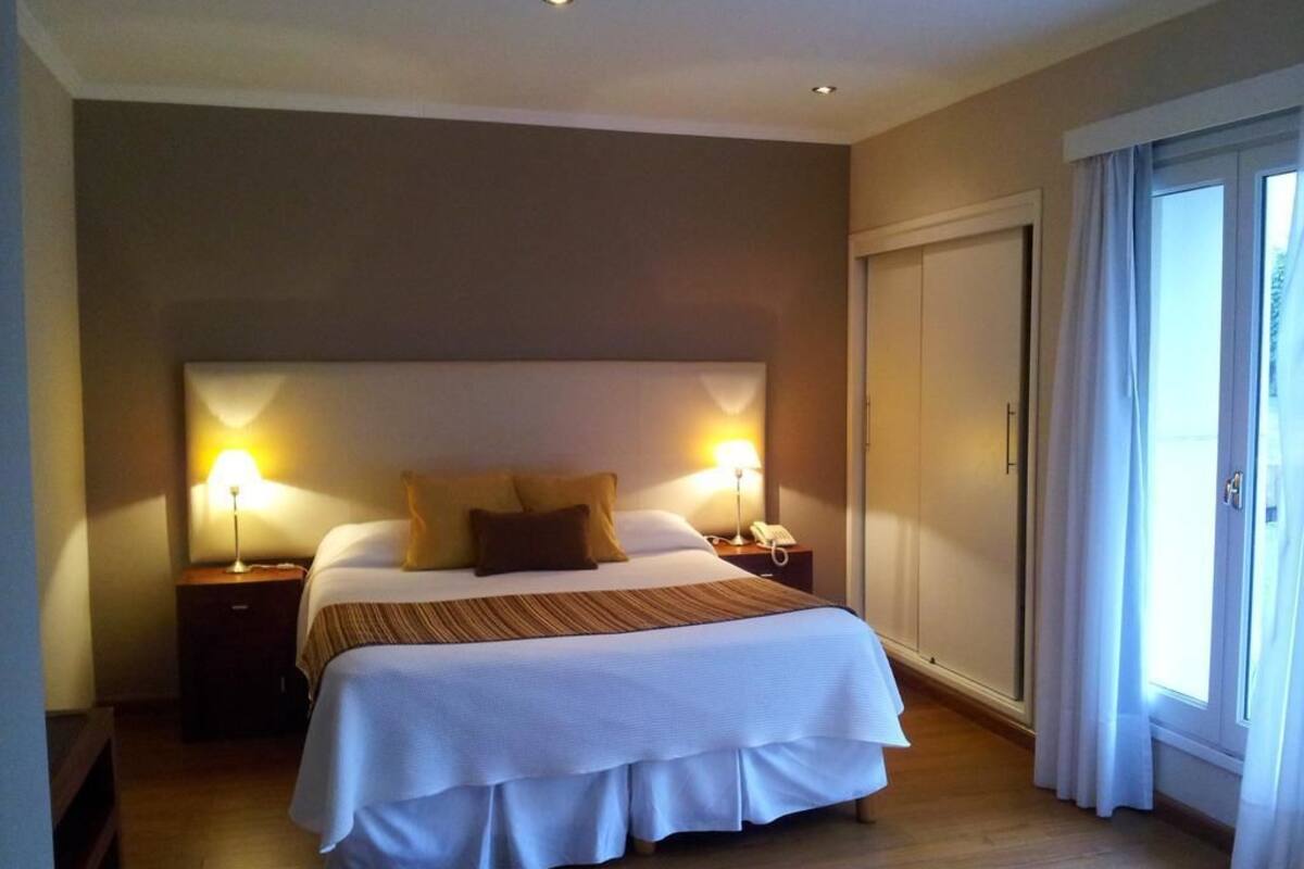 A hotel room with a large bed, two bedside lamps, a nightstand, and a sliding door to the outside.