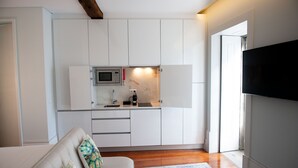 A modern kitchen with white cabinets, a microwave, and a sink. There is a flat-screen TV mounted on the wall to the right. - Guimarães IN (Guimarães)