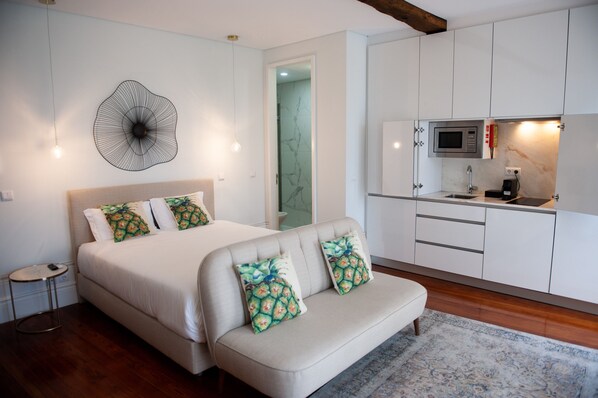A bedroom with a bed, a sofa, a small table, and a kitchenette with a microwave and sink. - Guimarães IN (Guimarães)