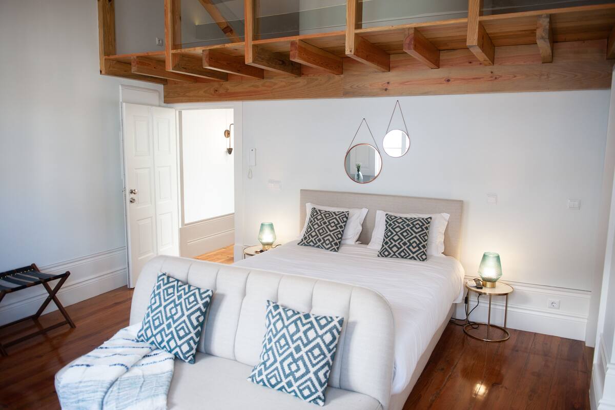 A bedroom with a bed, two bedside tables with lamps, a wooden ceiling, and a white door.