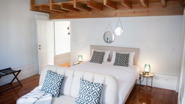 A bedroom with a bed, two bedside tables with lamps, a wooden ceiling, and a white door. - Guimarães IN (Guimarães)