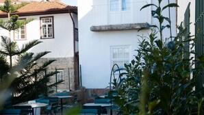 A courtyard with outdoor seating, a white building with a red-tiled roof, and a stone wall. - Guimarães IN (Guimarães)