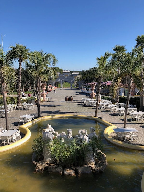 A courtyard with a central fountain surrounded by palm trees and outdoor seating.