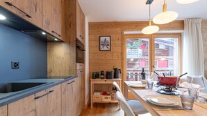 A modern kitchen with wooden cabinets, a black countertop, and a dining area with a wooden table and chairs. - Pracondu 1 407 - OUTDOOR & FUN  apartment 6 pers (Haute-Nendaz)