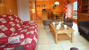 Ein gemütliches Wohnzimmer mit einem gemusterten Sofa, einem Holztisch und einem Essbereich mit Stühlen.