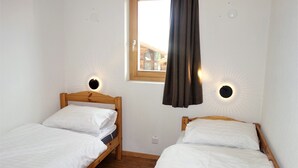 Ein Zimmer mit zwei Holzbetten, weißer Bettwäsche, einem Fenster mit Blick und Wandleuchten.