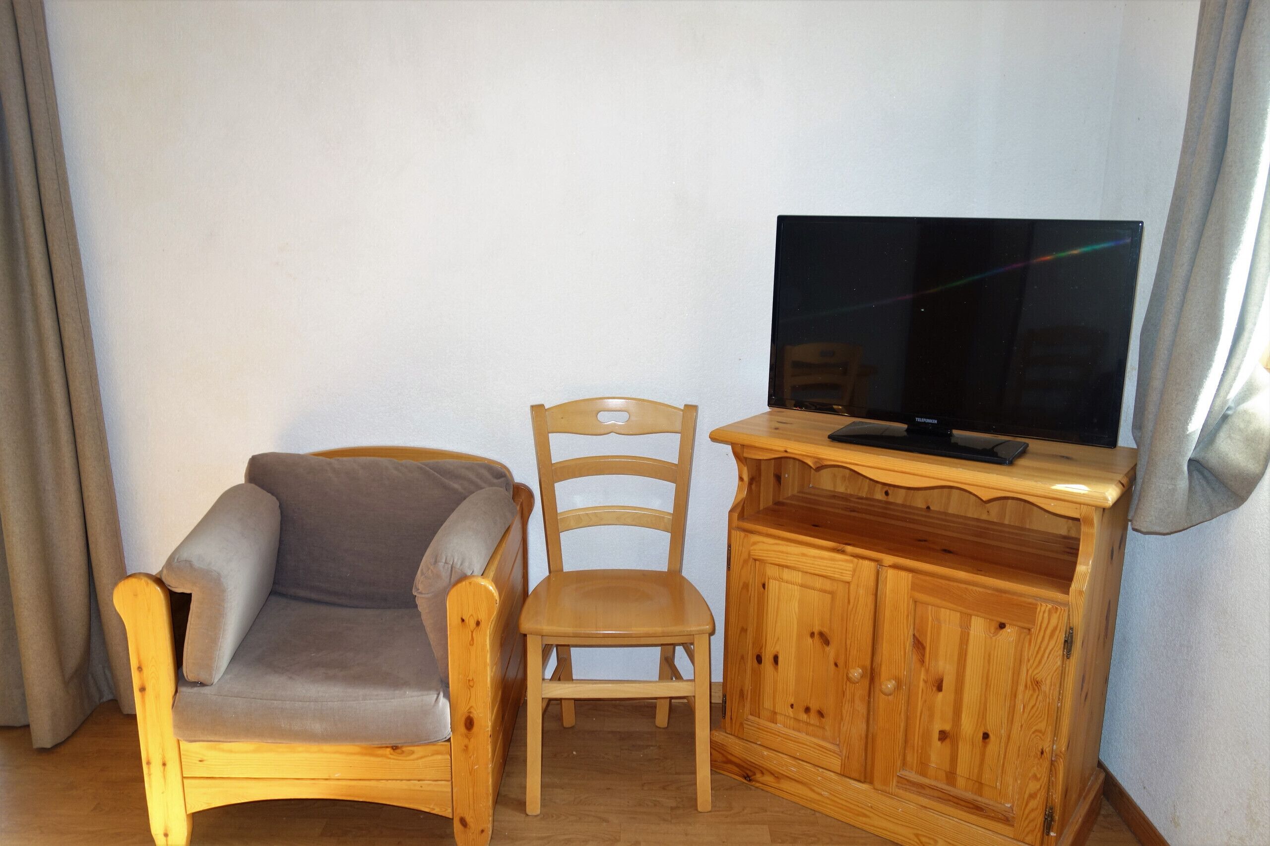 A room with a wooden chair, a sofa, and a TV on a wooden cabinet.