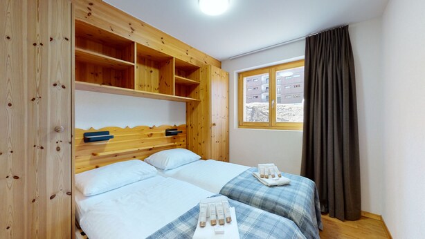 A bedroom with two beds, wooden headboards, a window with curtains, and a view of buildings outside. - Pracondu 1 A01 - OUTDOOR & FUN  charming apartment (Haute-Nendaz)