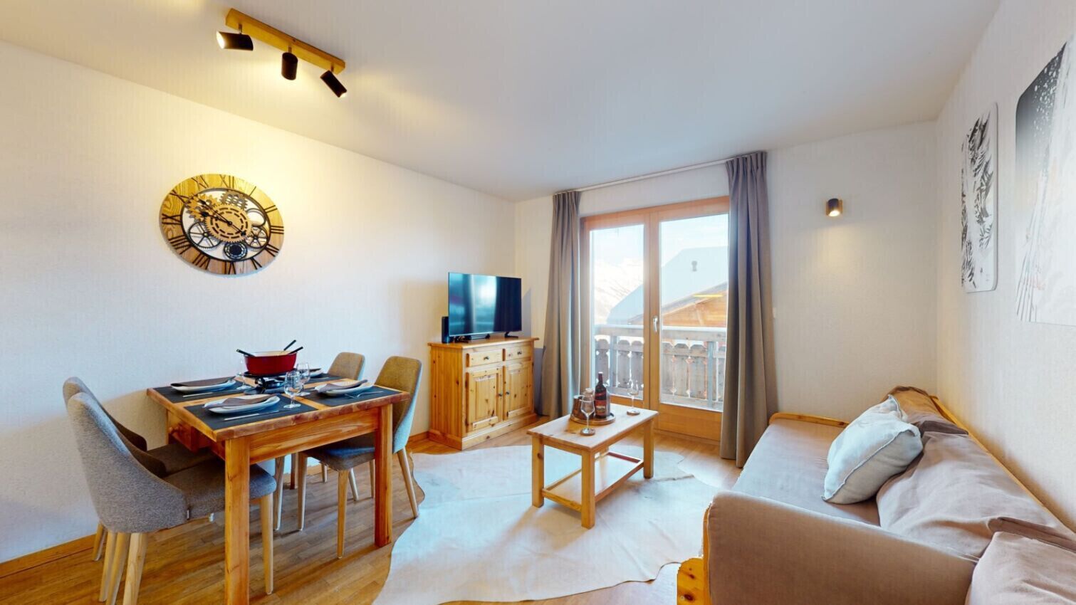 A living room with a wooden dining table, a sofa, a TV, and a balcony with curtains.