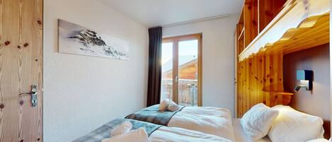 Een hotelkamer met twee bedden, een houten deur, een raam met uitzicht op bergen en een schilderij aan de muur.