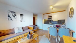 Een moderne woonkamer met een bank, een eettafel met stoelen, en een keuken met kasten en apparatuur.