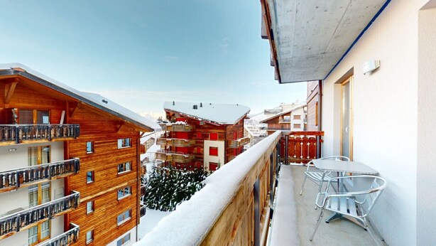 Een balkon met uitzicht op omliggende gebouwen, een tafel met stoelen en een met sneeuw bedekte grond.
