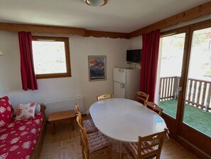 A cozy room with a round table, wooden chairs, a sofa, and a window with curtains.