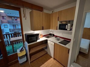 Una cocina compacta con armarios de madera, un microondas, un fregadero y un lavavajillas.