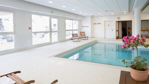 Una piscina interior con sillas reclinables de madera y una planta en maceta.
