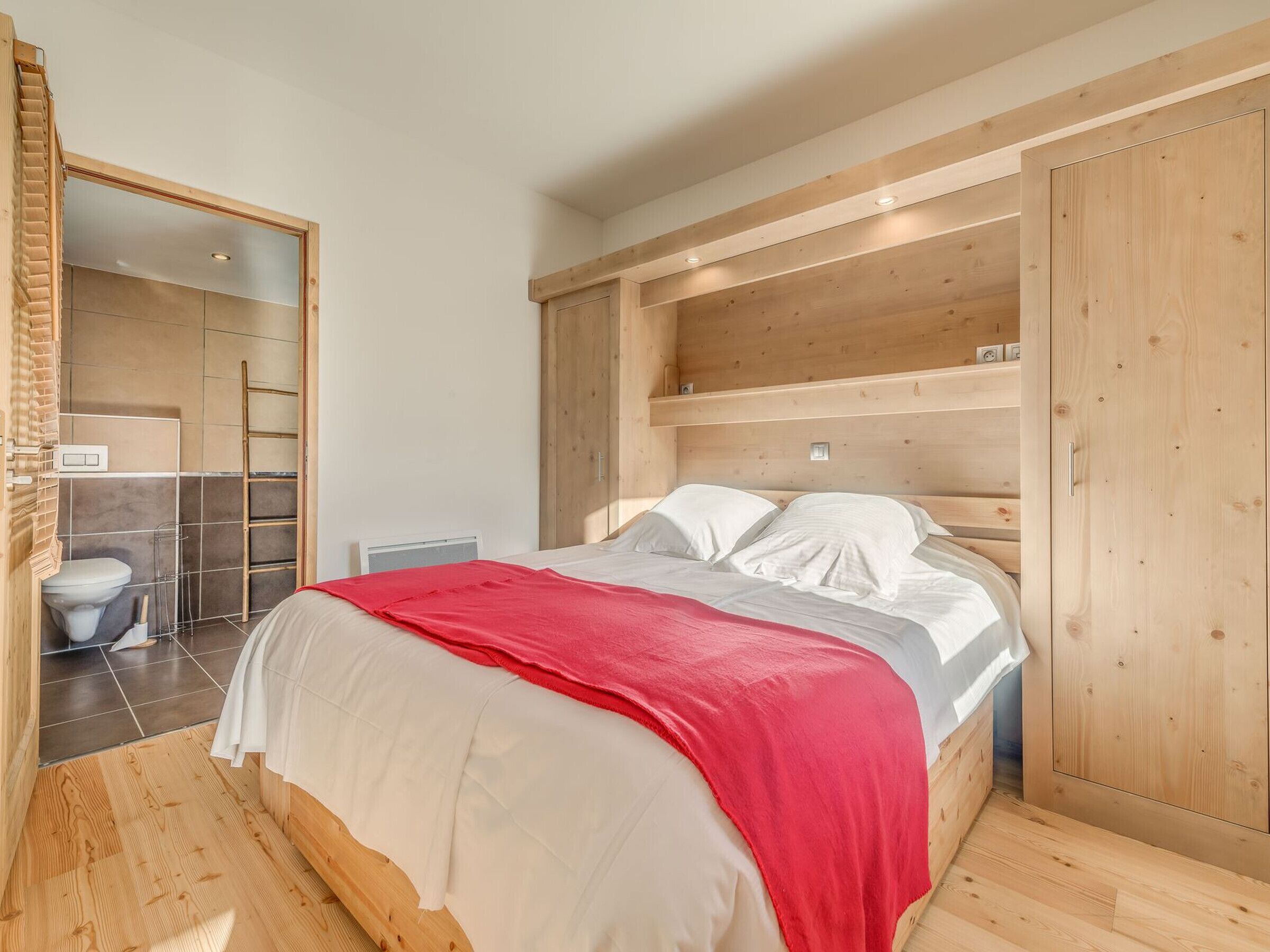 Un dormitorio con una cama de madera, una manta roja y un armario de madera.
