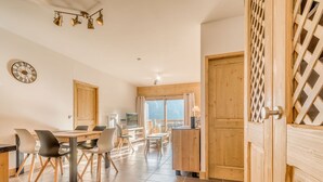 Una cocina moderna con armarios de madera, un comedor con sillas, un reloj y vistas a un balcón.