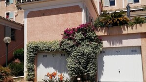 Un immeuble résidentiel doté d’un portail de garage, d’un petit jardin avec des plantes et d’une barrière métallique.