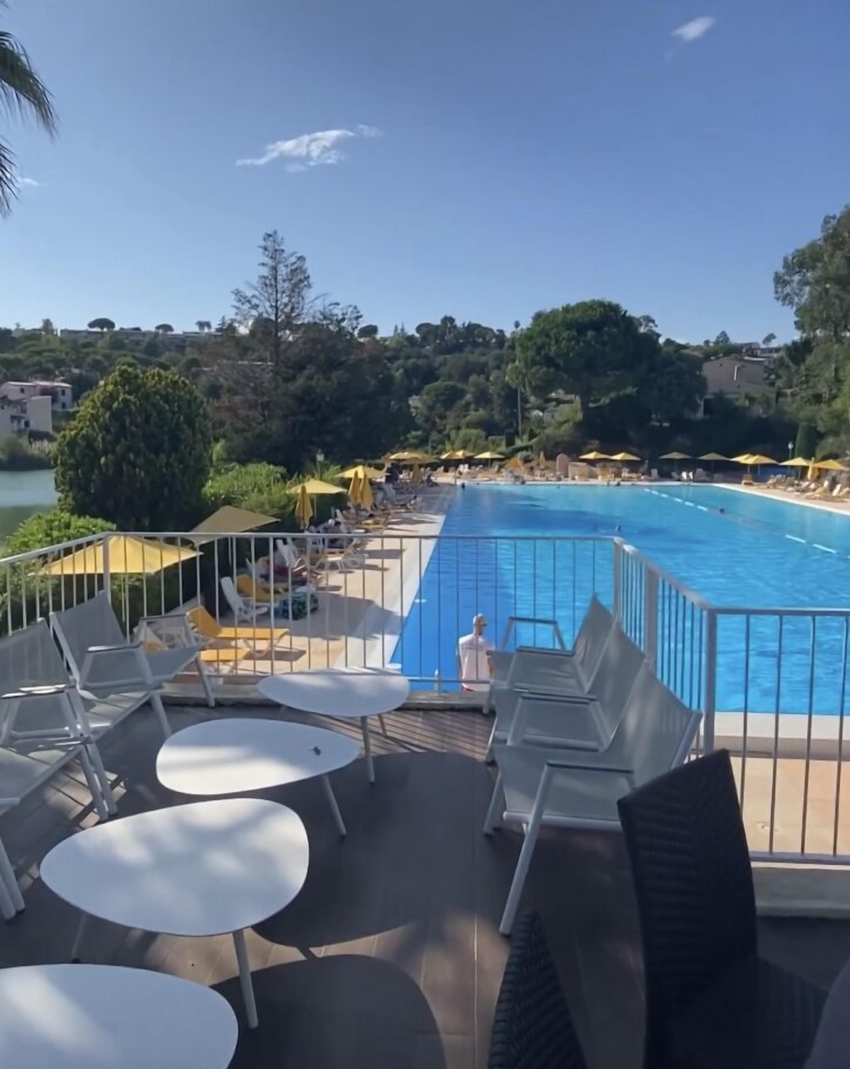 Un área junto a la piscina con sillones de descanso y mesas, una piscina y vistas del paisaje circundante.