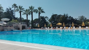 Une piscine à l’eau d’un bleu cristallin, entourée de chaises longues et de parasols, avec des palmiers en arrière-plan.
