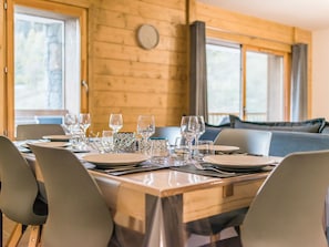 Una mesa de comedor con platos, vasos y cubiertos en una habitación con paredes de madera y ventanas amplias.