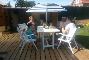A wooden deck with a white table and chairs under a striped umbrella.