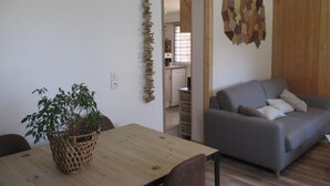 Een woonkamer met een grijze bank, een houten eettafel met stoelen en een potplant.