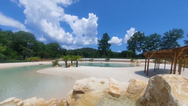 Ein klares Schwimmbecken mit einer Holzterrasse und einem Sandstrand.