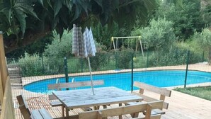 Eine Holzterrasse mit Billardtisch und Bänken, umgeben von viel Grün und einem Schwimmbad.