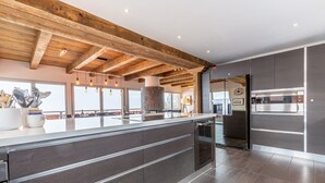 Une cuisine moderne dotée d’un grand îlot central, de meubles de couleur sombre et de poutres apparentes en bois.