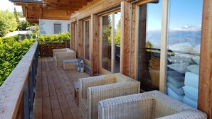 Une terrasse en bois, meublée de meubles en osier, et une porte vitrée donnant sur une vue imprenable sur les montagnes.