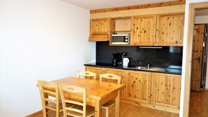 Une cuisine compacte avec des meubles en bois, un plan de travail noir, un four à micro-ondes, une machine à café et une table à manger avec des chaises.