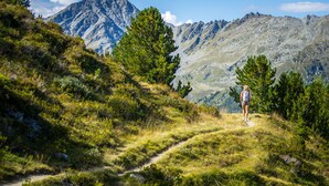 Un randonneur sur un sentier de montagne, dans un environnement accidenté, avec des montagnes lointaines se découpant sur un ciel dégagé.