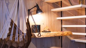 A room with a hanging light fixture, a desk with a lamp, and shelves against a wooden wall. - Bay Terminus - The Hanging Lodge (Saint-Blimont)