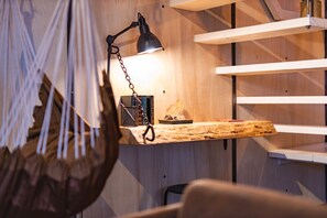 A wooden desk with a hanging lamp, a chair, and a shelf with books and a basket.