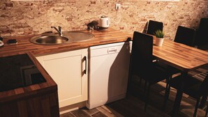 Een kleine keuken met een spoelbak, vaatwasser en een houten eettafel met stoelen.